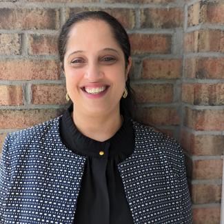 Saraswathi Bellur smiles wearing a patterned blue jacket in front of a brick wall