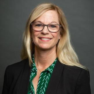 Lisa Parks smiles wearing glasses, a green button up shirt and black blazer