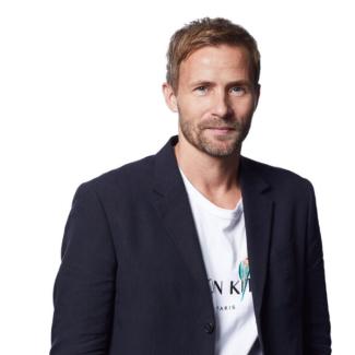 Mikkel Flyberbom poses in a black blazer and white tee shirt against a white background