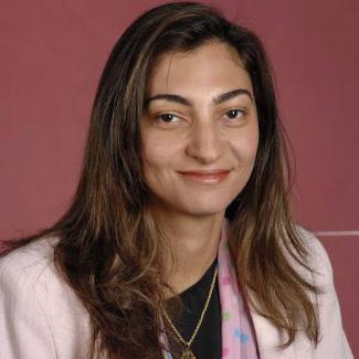 Rasha Abdulla smiles wearing a light pink blazer against a dark pink background