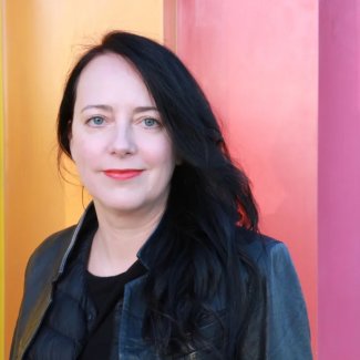 Ulrike Klinger poses in a black leather jacket against a colorful background